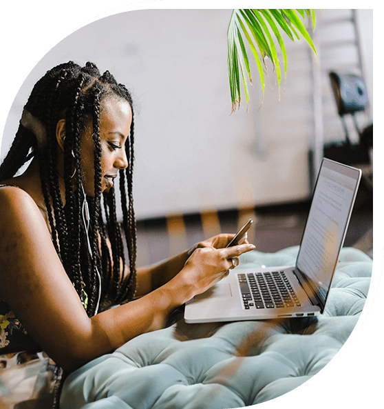 A woman is on her phone and using the laptop.