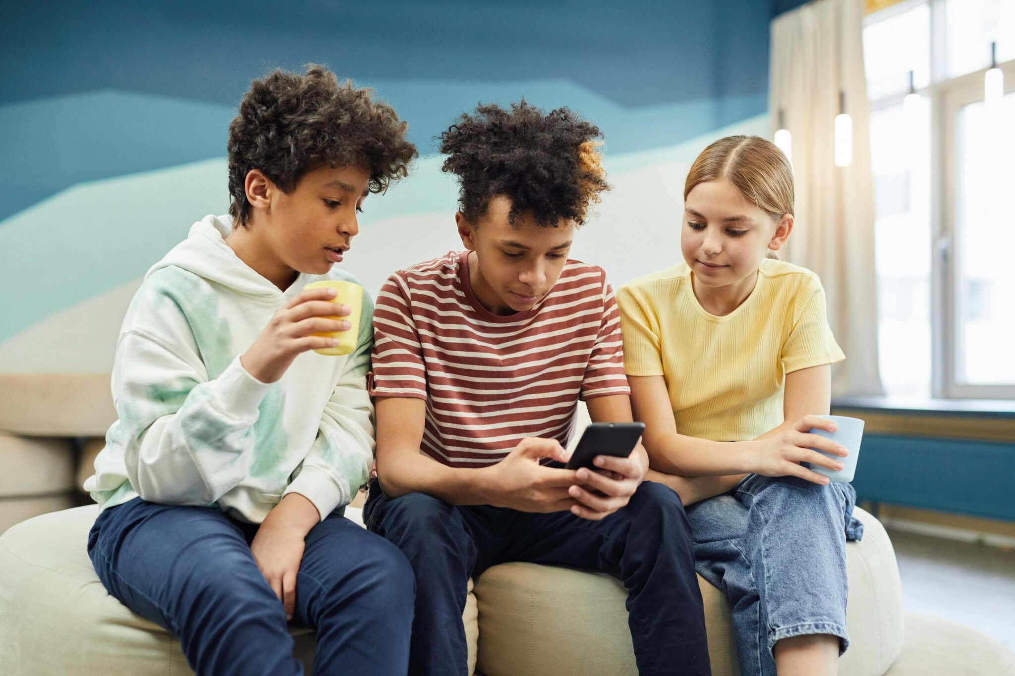 Three young people sitting on a couch looking at an iphone.