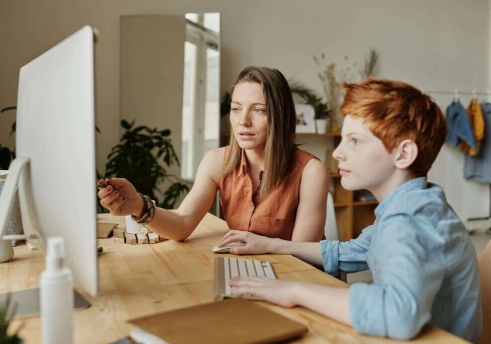 A woman and boy sitting at a table with a computer.