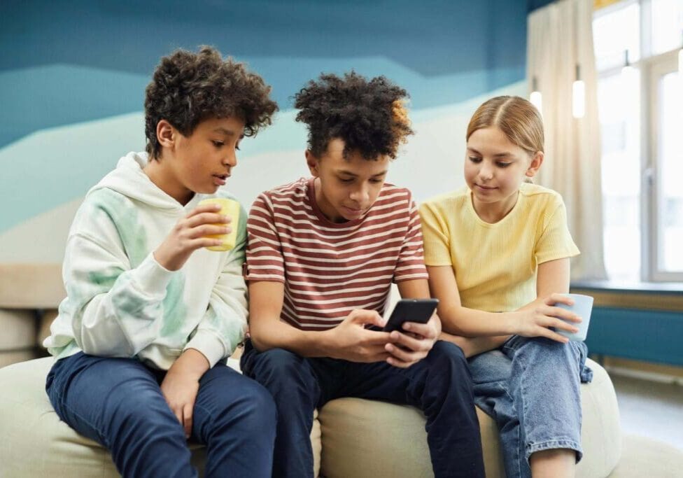 Three young people sitting on a couch looking at an iphone.